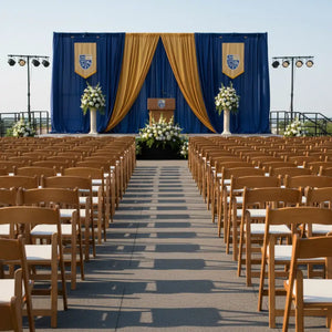 Empty outdoor ceremony setup with chairs, floral arrangements, and a stage draped in blue and gold.